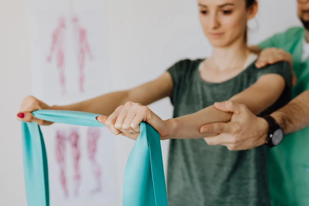 A healthcare professional guiding an adult through a resistance-band arm exercise.