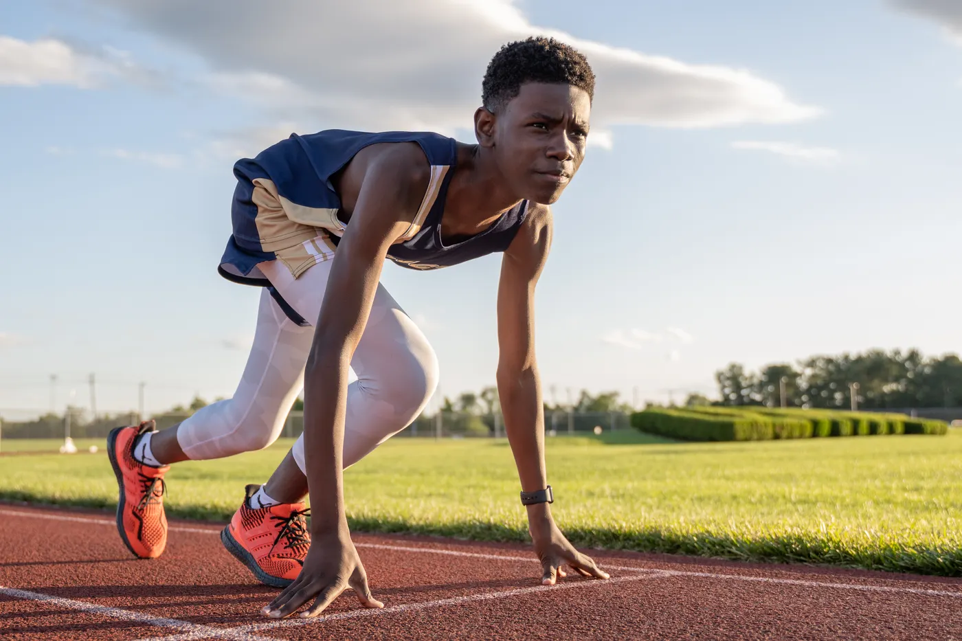 A runner crouched at the starting line on an outdoor track.