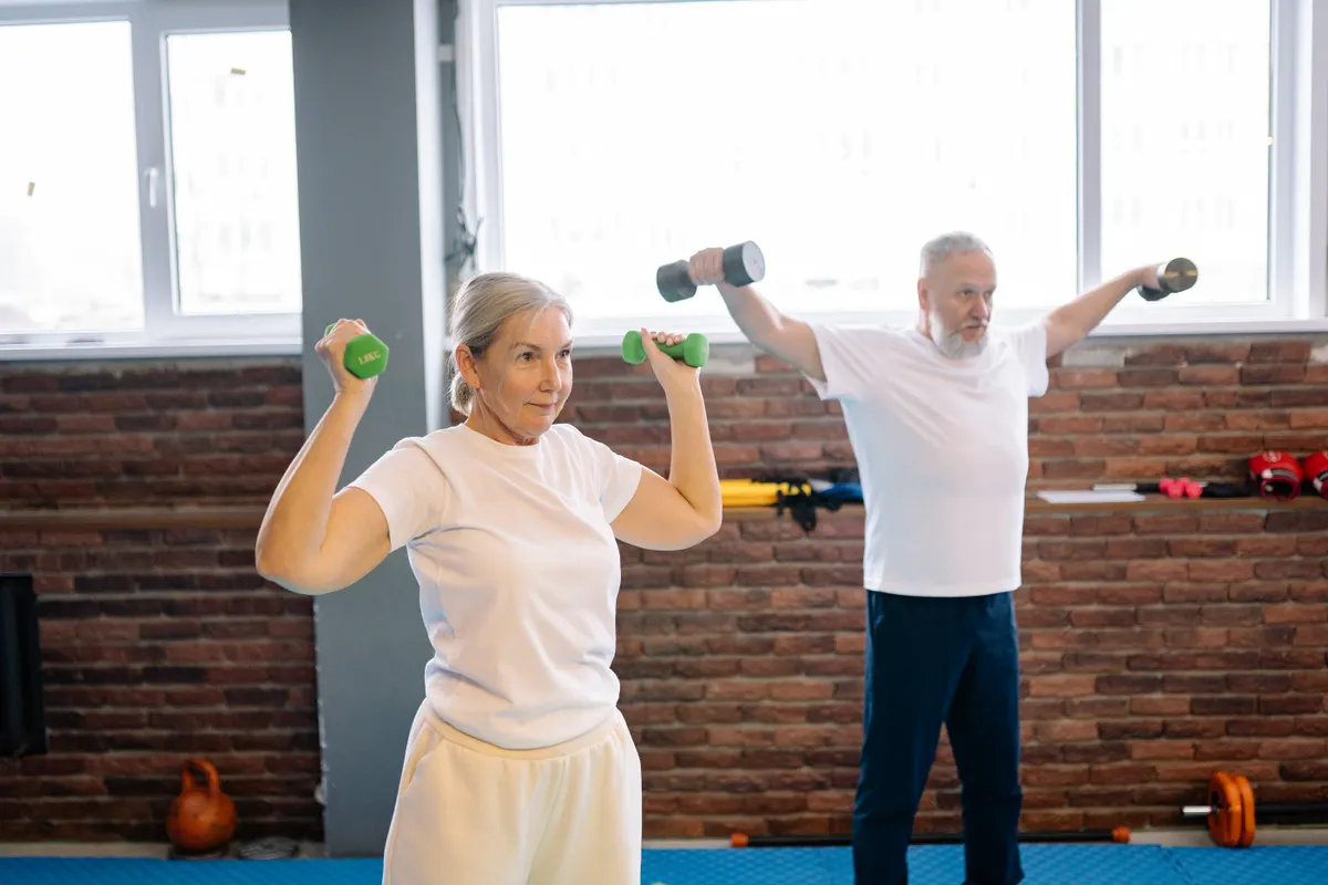 An older couple training with light dumbbells in a gym.